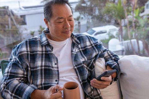 Senior Man Relaxing on Sofa with Smartphone and Coffee