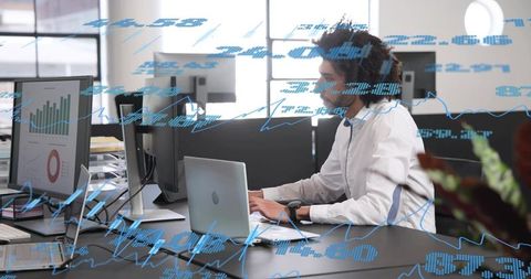 Analyzing financial dashboards on laptop and dual monitors in modern open office