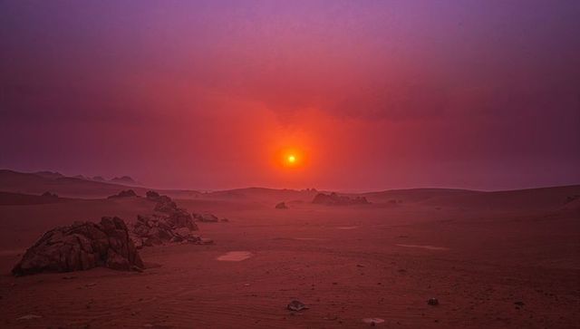 Glowing low sun casting warm light across desert plain at dusk with rock outcrops, haze