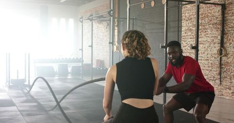Trainer guiding trainee through intense battle rope exercise