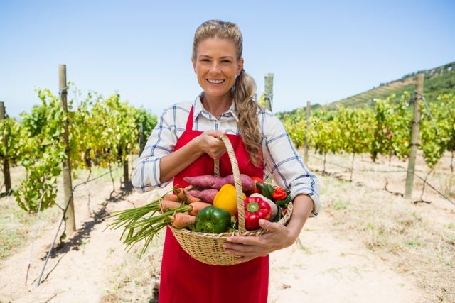 Portrait of happy woman holding a basket of fresh vegetables in vineyard