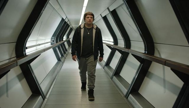 Young man walking futuristic glass walkway wearing hoodie and pendant, urban symmetry