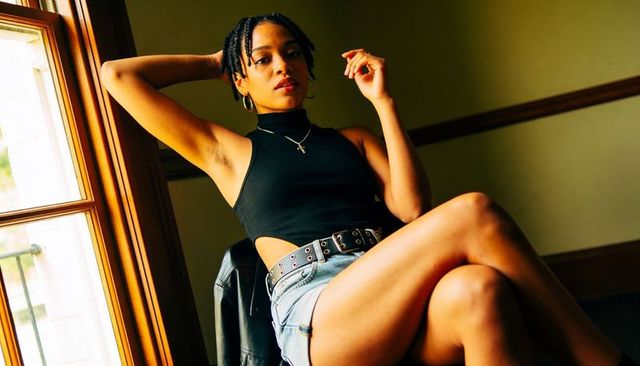 Sunlit fashion portrait of model leaning by window wearing black top and denim shorts