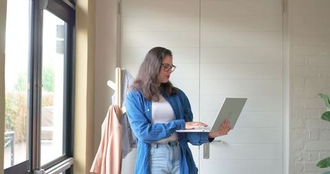 Young woman standing in entryway holding laptop, working in minimalist home office