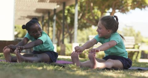 Schoolgirls stretching on mats during outdoor yoga class on sunny campus lawn promoting friendship