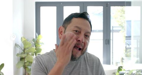 Middle-aged asian man applying facial cream in morning grooming in bright bathroom