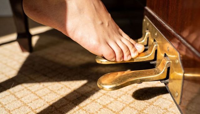 Bare foot pressing brass piano pedal close-up sunlight on patterned carpet