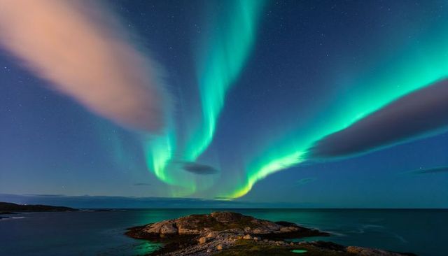 Aurora borealis dancing above rocky coastal islet reflecting in tidal pools