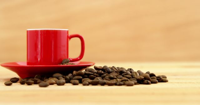Red ceramic coffee cup sits on matching saucer with coffee beans spilled on light wooden table. Ideal for advertising coffee shops, illustrating morning routines, and promoting coffee products or breakfast menus.