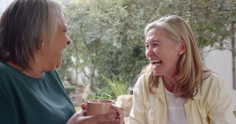 Smiling Female Friends Enjoying Coffee and Laughter in Relaxing Backyard