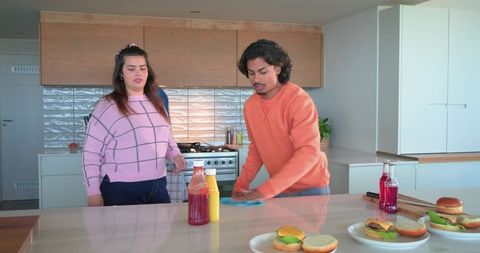 Young couple wiping kitchen island and assembling burgers in bright modern home kitchen
