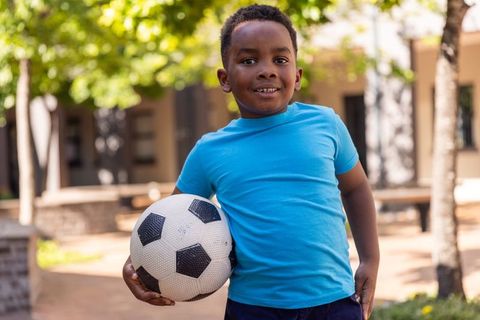 African american boy holding soccer ball in sunlit courtyard smiling and ready to play