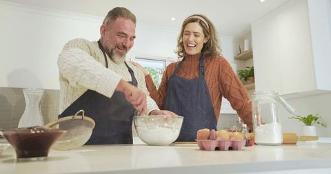 Cheerful couple mixing dough together in sunny kitchen