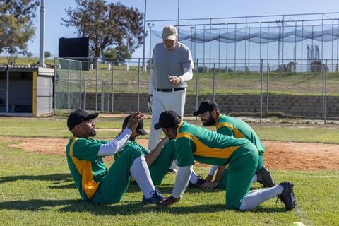 Coach guiding baseball team while teammates supporting seated player during practice
