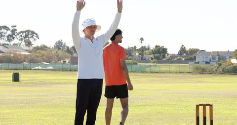 Umpire signaling six as indian bowler bowling underarm, teammate walking on cricket field