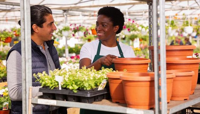 Greenhouse staff guiding customer selecting terracotta pots and seedlings at nursery retail