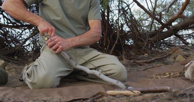 Man kneeling on ground practicing primitive fire starting techniques in a wilderness setting. Ideal for content focused on survival skills, outdoor adventures, bushcraft tutorials, and nature expeditions.