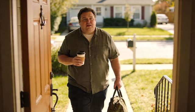Returning home carrying coffee and duffel bag, entering suburban front doorway at morning