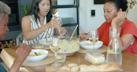 Multigenerational women sharing casual home dinner around wooden table with pasta salad