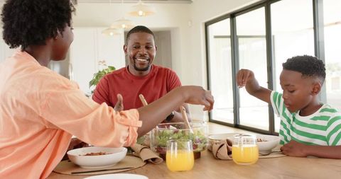 African american family sharing healthy meal, parents and son serving salad at dining table