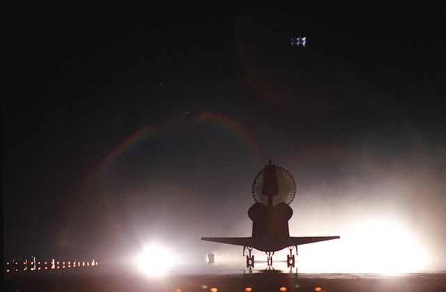 With its drag chute billowing behind, Space Shuttle Atlantis is silhouetted against the bright lights on Runway 15, Shuttle Landing Facility, as it rolls to a stop. Two rainbows appear above the lights. The landing of Atlantis completed the 9-day, 20-hour, 9-minute-long STS-101 mission. At the controls are Commander James D. Halsell Jr. and Pilot Scott 'Doc' Horowitz. Also onboard the orbiter are Mission Specialists Mary Ellen Weber, James S. Voss, Jeffrey N. Williams, Susan J. Helms and Yury Usachev of Russia. Main gear touchdown was at 2:20:17 a.m. EDT, landing on orbit 155 of the mission. Nose gear touchdown was at 2:20:30 a.m. EDT, and wheel stop at 2:21:19 a.m. EDT. The crew is returning from the third flight to the International Space Station. This was the 98th flight in the Space Shuttle program and the 21st for Atlantis, also marking the 51st landing at KSC, the 22nd consecutive landing at KSC, the 14th nighttime landing in Shuttle history and the 29th in the last 30 Shuttle flights. 