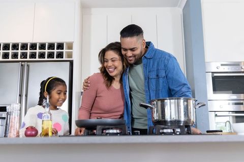 Family cooking together on kitchen island, parents guiding daughter, modern home moments