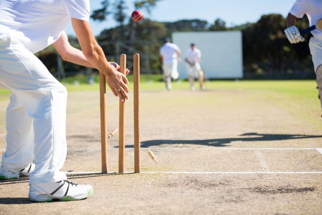 Wicket keeper hitting stumps during a cricket match on a sunny day. Ideal for use in sports articles, cricket training materials, and promotional content for cricket events. Highlights the action and excitement of the game.