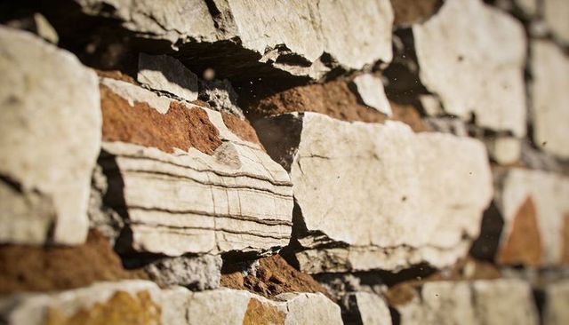 Close-up dry-stacked stone wall revealing bedding lines, sunlit dust and layered slabs