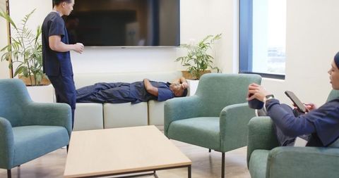 Healthcare team resting and chatting in sunlit staff lounge wearing navy scrubs on break