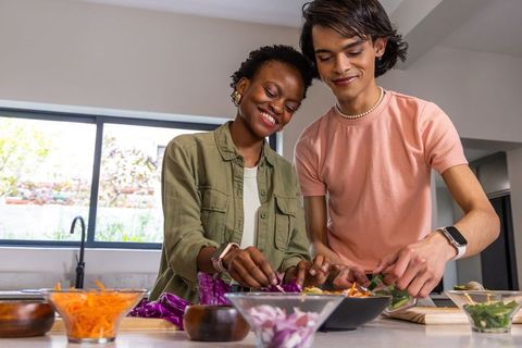 African american woman and asian man preparing fresh salad together at kitchen island