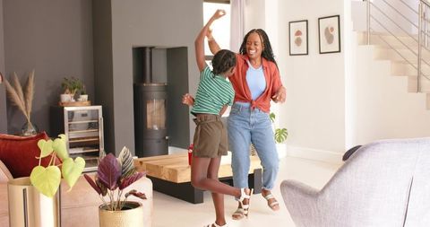 Mother and child dancing together in bright minimalist living room with plants and wood