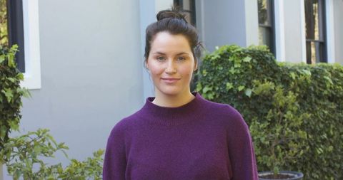 Standing midlife woman wearing purple knit sweater with hair bun in courtyard