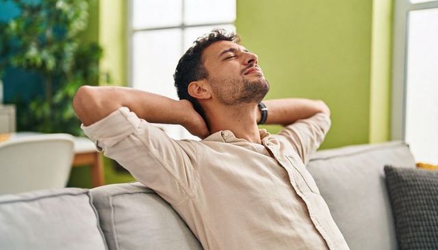 Relaxing man reclining on sofa wearing wristwatch in bright green living room interior