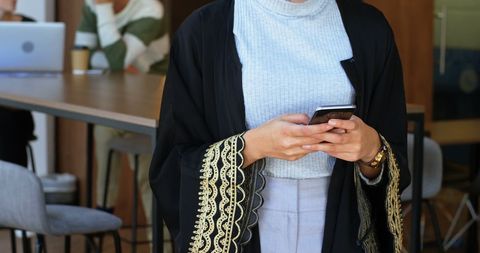Businesswoman in Traditional Abaya Using Smartphone in Modern Cafe