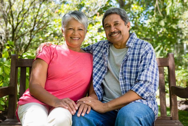 Senior couple sitting together in garden on a sunny day, smiling and enjoying each other's company. Ideal for use in advertisements, brochures, or articles related to retirement, senior living, family, and outdoor activities.
