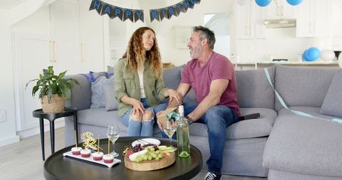 Mature Couple Celebrating Birthday with Gifts and Food on Sofa