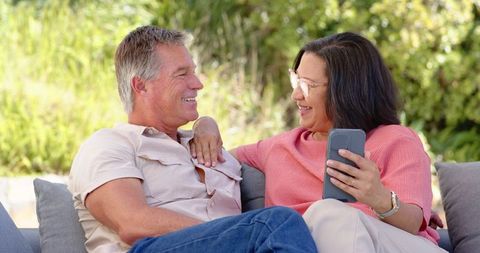 Senior Couple Relaxing Outdoors with Smartphone in Lush Garden