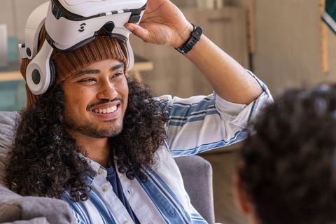 Diverse friends enjoying vr gaming at home smiling man lifting white headset wearing beanie