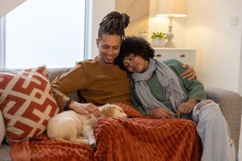 Couple cuddling on sofa while petting sleeping puppy under rust-orange cozy blanket