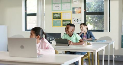 Diverse middle school students using tablets and laptops in bright classroom learning