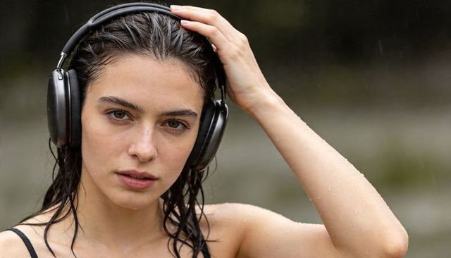Woman adjusting headphones with wet hair on coastal shoreline, serene close-up