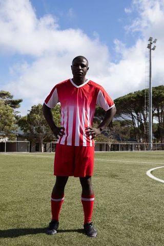 Soccer player standing confidently on turf field in red uniform