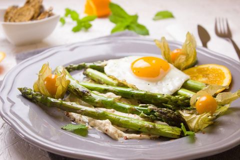 Serving grilled asparagus with sunny-side up egg, cape gooseberry and orange