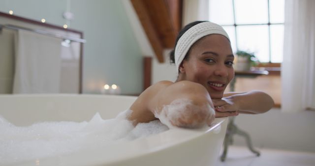 Portrait of biracial woman taking a bath looking at camera and smiling. domestic life, spending quality free time relaxing at home.