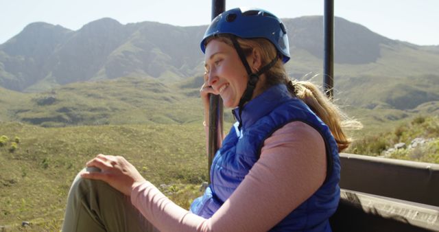 Adventurous woman smiling while exploring mountain trails, wearing a blue helmet and vest. Suitable for travel brochures, outdoor adventure promotions, hiking gear advertisements, and nature blog illustrations.