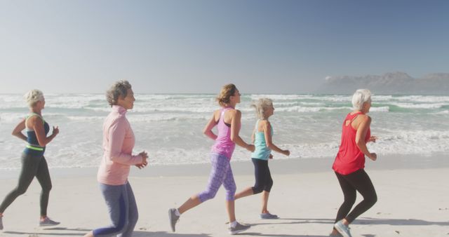 Group of women running on a beach near the ocean on a sunny day. Perfect for content related to fitness, healthy lifestyle, senior activities, group exercises, outdoor workouts, and promoting wellness. The setting evokes feelings of camaraderie, health, and the benefits of outdoor exercise.