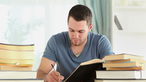 Focused Writer Examining Notes Surrounded by Stacks of Books