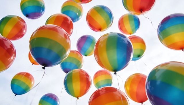 Floating rainbow balloons drifting upward in bright sky, festive colorful helium spheres