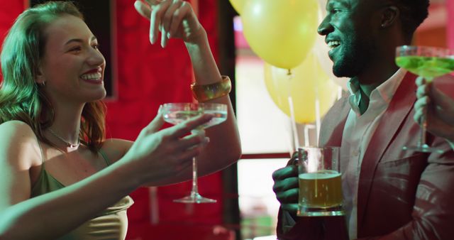 Image of diverse group of happy friends laughing, drinking and making a toast at a nightclub bar. Friendship, going out and socialising concept.