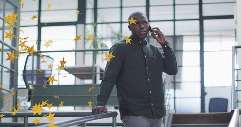 Executive speaking on phone while leaning on railing in modern atrium with gold confetti